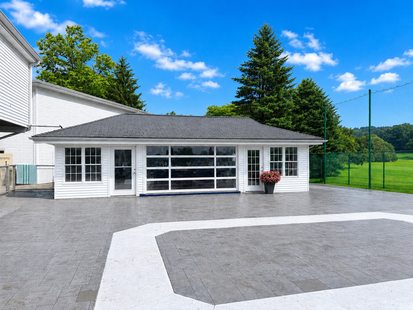 The Pool Cabana at Brownson Country Club, a white pavilion with large glass doors and windows on a patterned concrete patio under a bright blue sky